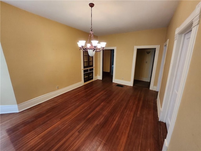 empty room with a chandelier, visible vents, baseboards, and dark wood-style floors