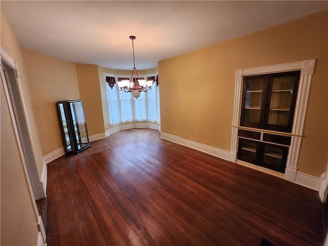 unfurnished dining area featuring a notable chandelier, baseboards, and dark wood-style floors