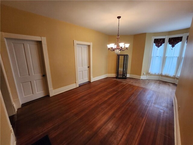 unfurnished dining area with a chandelier, baseboards, and dark wood finished floors
