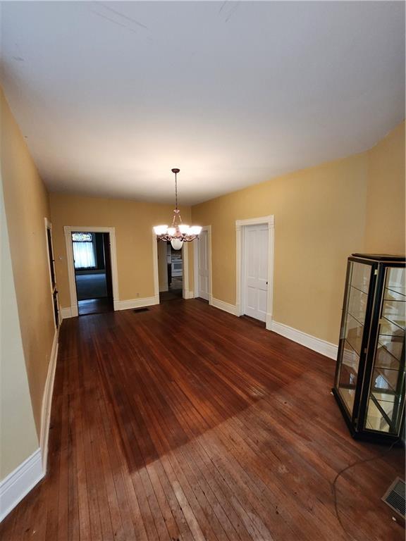 unfurnished dining area featuring a chandelier, dark wood-type flooring, baseboards, and visible vents