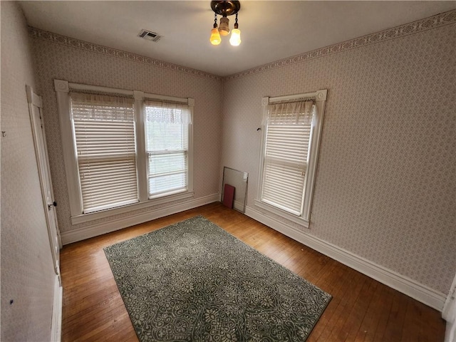 empty room with hardwood / wood-style flooring, visible vents, baseboards, and wallpapered walls