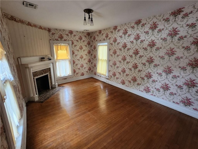 unfurnished living room featuring baseboards, wallpapered walls, visible vents, hardwood / wood-style floors, and a high end fireplace