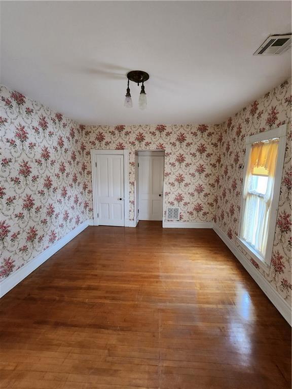 spare room with visible vents, baseboards, wallpapered walls, and wood finished floors