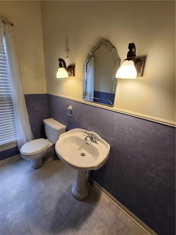 bathroom with toilet, a sink, and a wainscoted wall