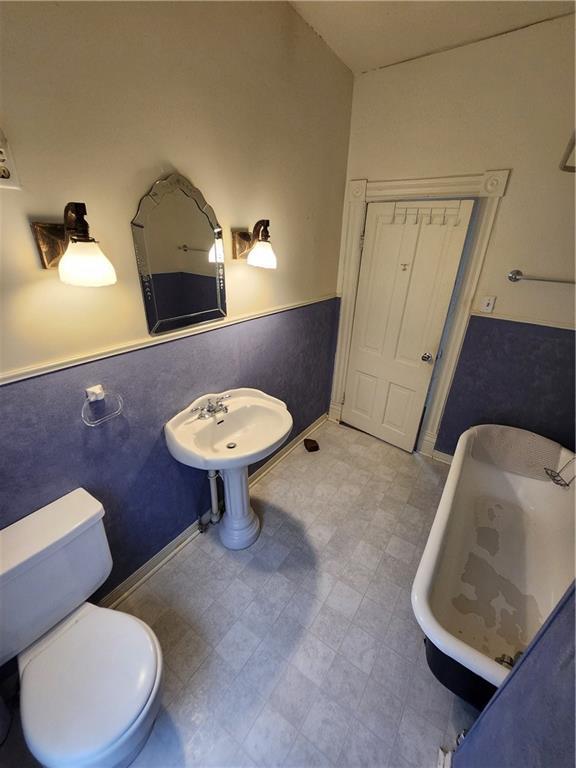 bathroom featuring toilet, a freestanding bath, and wainscoting
