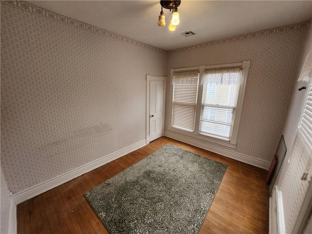 empty room with visible vents, baseboards, hardwood / wood-style flooring, and wallpapered walls