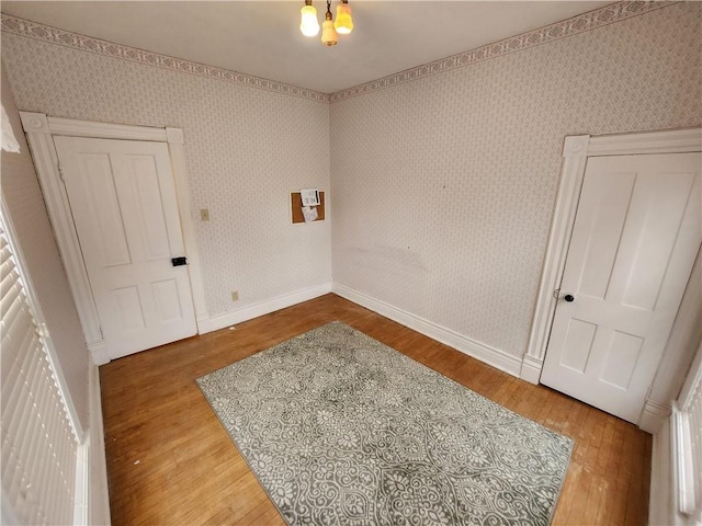 unfurnished room with baseboards, wood finished floors, and wallpapered walls