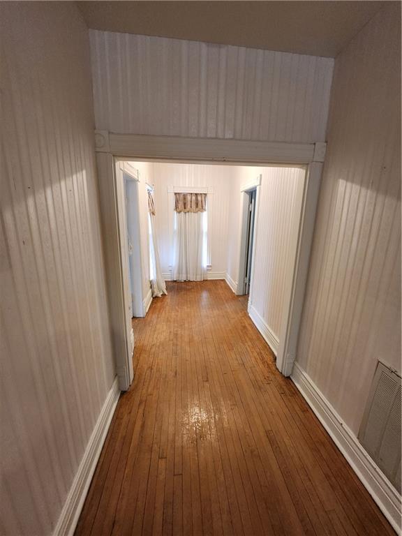 corridor with wood-type flooring, baseboards, and visible vents