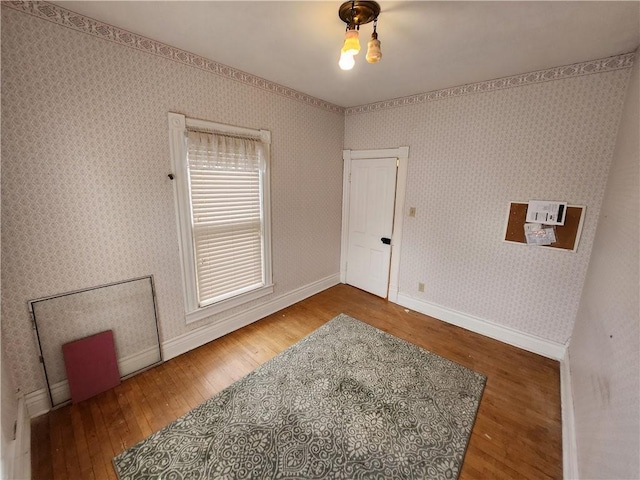 spare room with wallpapered walls, wood-type flooring, and baseboards