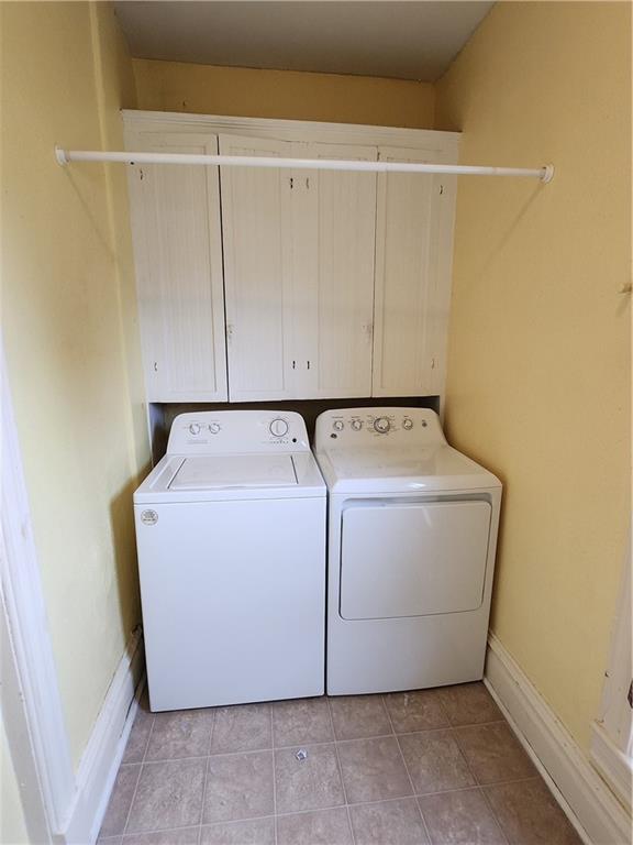 laundry area featuring light tile patterned floors, baseboards, cabinet space, and washing machine and dryer