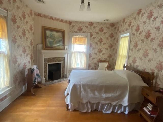 bedroom featuring visible vents, light wood-type flooring, a fireplace, and wallpapered walls