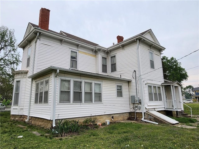 back of property with entry steps, a lawn, and a chimney