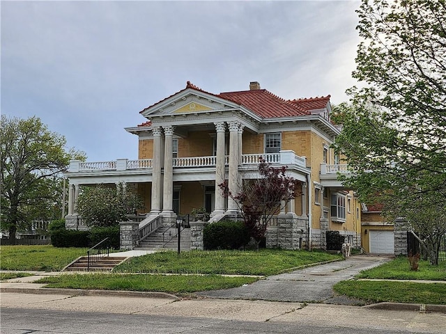 greek revival inspired property with a balcony, stone siding, aphalt driveway, a tile roof, and a garage