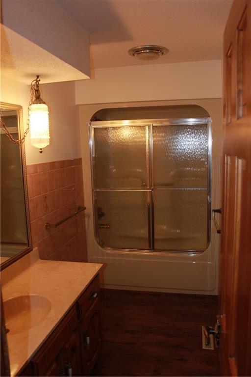 1410 Grandview Dr, Warrensburg, MO 64093 - full bathroom with tile walls, bath / shower combo with glass door, vanity, and wood finished floors