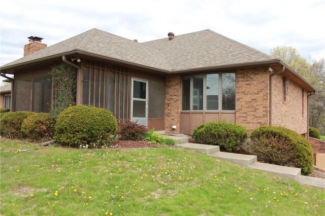 1410 Grandview Dr, Warrensburg, MO 64093 - view of front of home featuring a chimney, brick siding, a front lawn, roof with shingles, and a sunroom