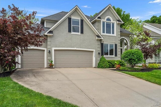 traditional home with stucco siding, concrete driveway, an attached garage, and a shingled roof