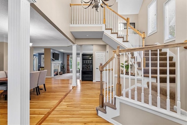 stairs featuring wood finished floors, a high ceiling, a chandelier, ornate columns, and a warm lit fireplace