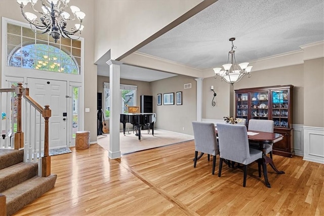 dining area with a chandelier, light wood-style flooring, ornate columns, crown molding, and stairs