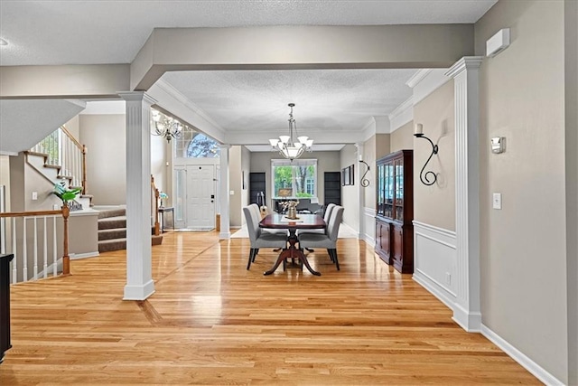 dining space with a chandelier, ornate columns, light wood finished floors, stairway, and ornamental molding