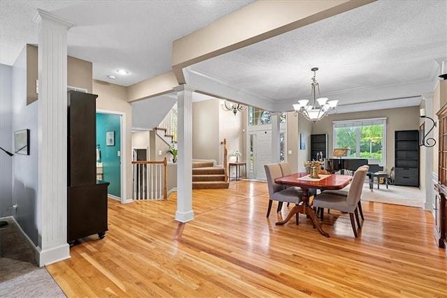 dining area featuring stairway, ornate columns, light wood-type flooring, a chandelier, and a textured ceiling
