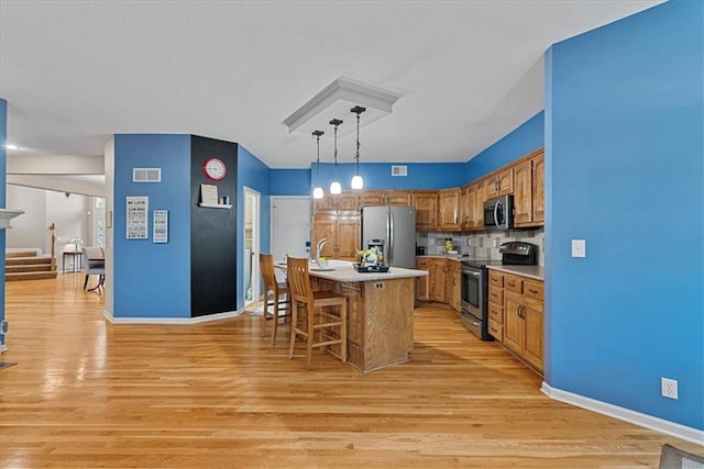 kitchen with stainless steel appliances, brown cabinets, light countertops, a kitchen bar, and light wood finished floors