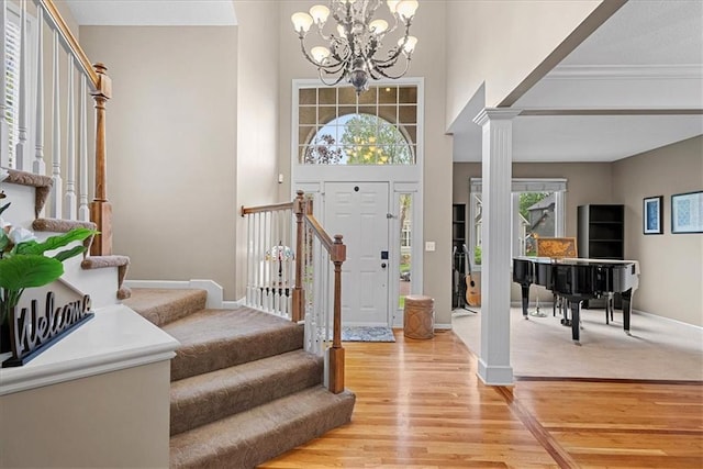foyer entrance with stairs, light wood-type flooring, a chandelier, ornate columns, and baseboards