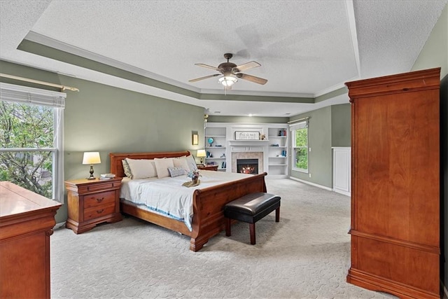 bedroom featuring light colored carpet, a textured ceiling, a raised ceiling, a lit fireplace, and ceiling fan