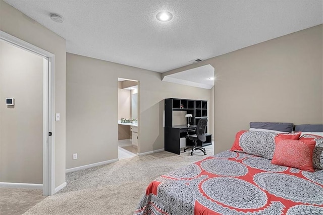 carpeted bedroom featuring an office area, a textured ceiling, baseboards, and ensuite bath