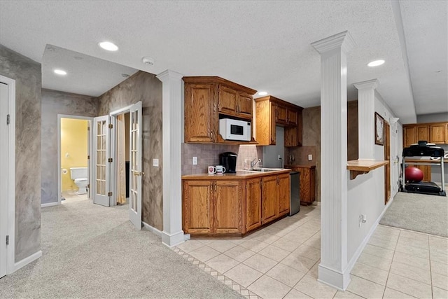 kitchen with white microwave, ornate columns, light colored carpet, brown cabinetry, and a textured ceiling