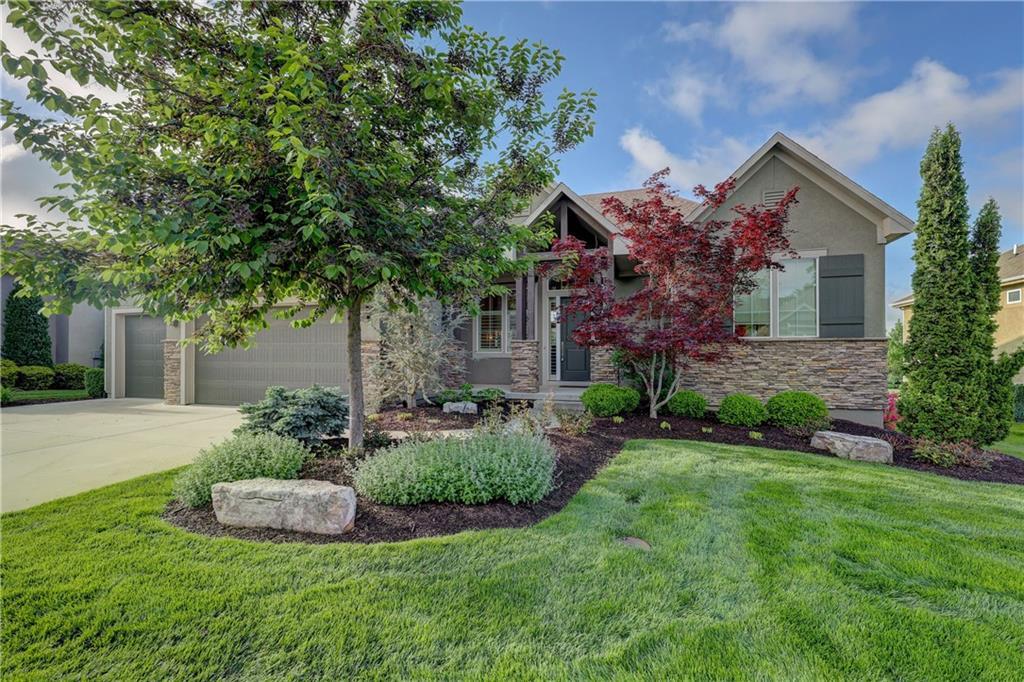 view of front of home with driveway, stucco siding, a front yard, and stone siding