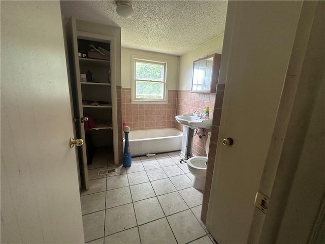 218 S Kent St, Excelsior Springs, MO 64024 - bathroom with tile walls, tile patterned floors, a textured ceiling, a bathtub, and a wainscoted wall