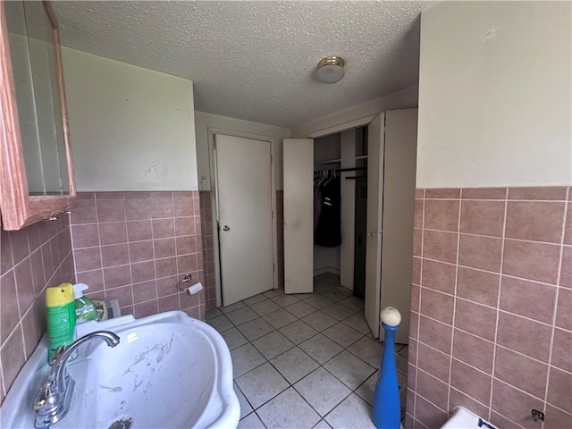 218 S Kent St, Excelsior Springs, MO 64024 - bathroom featuring tile walls, tile patterned flooring, a sink, a textured ceiling, and a wainscoted wall