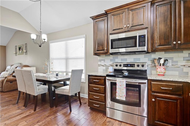 kitchen with vaulted ceiling, decorative backsplash, open floor plan, light wood finished floors, and appliances with stainless steel finishes