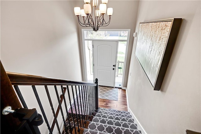 foyer featuring baseboards, wood finished floors, an inviting chandelier, and stairs