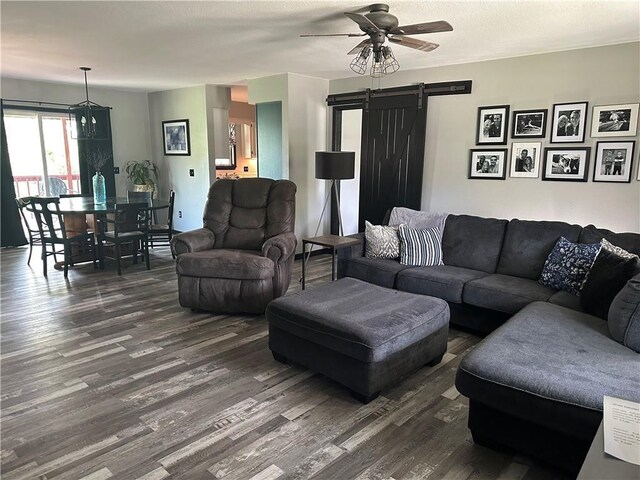 living room featuring dark wood-style flooring, a ceiling fan, and a barn door