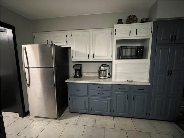 kitchen featuring black microwave, light countertops, white cabinetry, freestanding refrigerator, and gray cabinetry