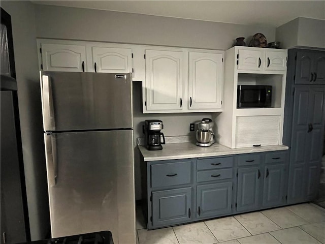 kitchen featuring white cabinets, light countertops, freestanding refrigerator, black microwave, and gray cabinetry