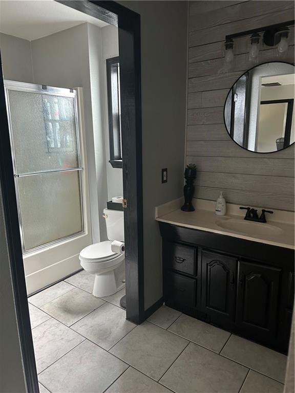 full bath with bath / shower combo with glass door, toilet, wooden walls, vanity, and tile patterned floors