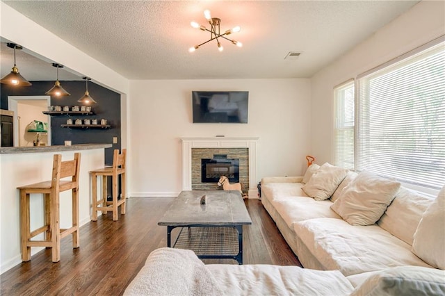 living room featuring dark wood-type flooring, a chandelier, a stone fireplace, baseboards, and a textured ceiling