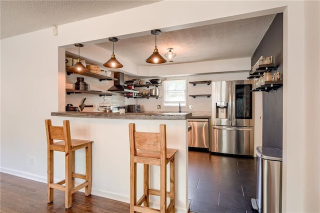 kitchen with appliances with stainless steel finishes, open shelves, wall chimney exhaust hood, a kitchen bar, and a peninsula