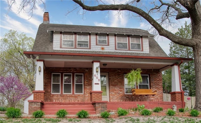 view of front of home featuring brick siding, a porch, a chimney, and a shingled roof