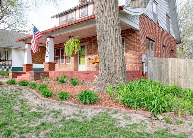 view of home's exterior with a chimney, brick siding, a porch, and fence