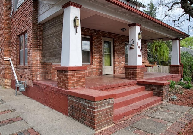 view of exterior entry featuring covered porch and brick siding