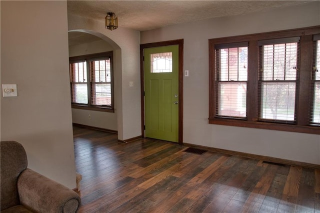 foyer featuring arched walkways, wood finished floors, visible vents, and baseboards