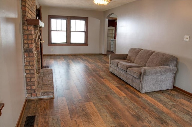 living area with arched walkways, wood finished floors, visible vents, and baseboards