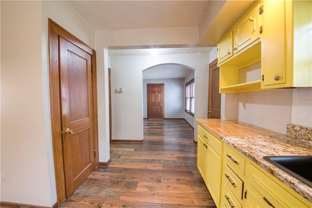 hall featuring arched walkways, baseboards, dark wood-type flooring, and a sink