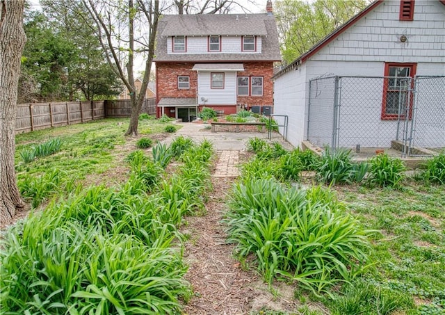 back of house with brick siding, roof with shingles, a chimney, and a fenced backyard