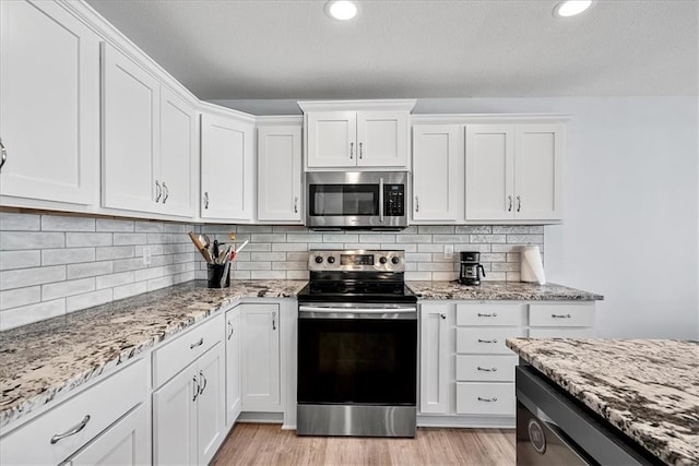 kitchen with white cabinetry, light wood finished floors, light stone countertops, and stainless steel appliances