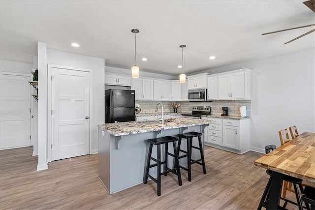 kitchen with decorative backsplash, white cabinetry, a sink, light wood-style flooring, and appliances with stainless steel finishes