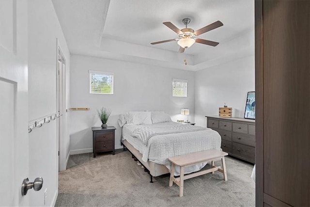 carpeted bedroom featuring baseboards, ceiling fan, a tray ceiling, and multiple windows